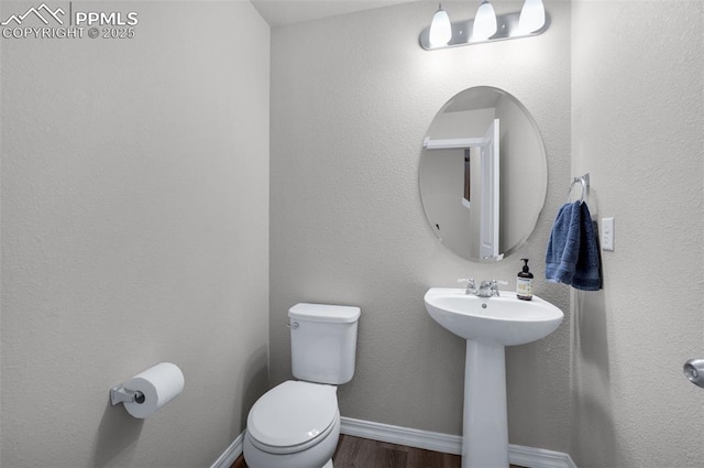 half bath featuring a sink, baseboards, toilet, and wood finished floors