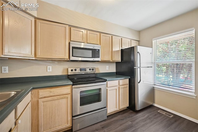 kitchen featuring light brown cabinetry, dark countertops, dark wood finished floors, stainless steel appliances, and visible vents