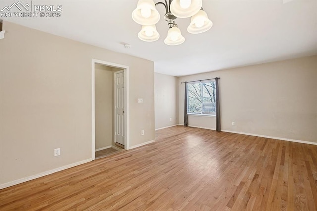 spare room featuring baseboards, a chandelier, and light wood-style flooring