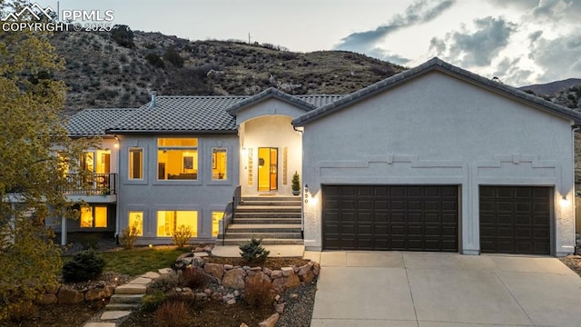 view of front facade with a tiled roof, driveway, a garage, a mountain view, and stucco siding