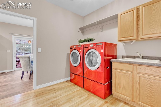 washroom featuring cabinet space, a sink, light wood finished floors, separate washer and dryer, and baseboards