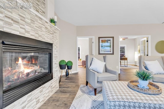 living area with a glass covered fireplace, baseboards, a ceiling fan, and wood finished floors