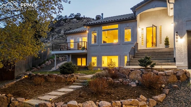 back of house featuring stairway, a balcony, a tile roof, and stucco siding