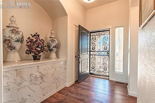 foyer featuring visible vents, baseboards, arched walkways, and dark wood-style floors