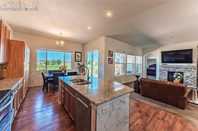 kitchen with dishwashing machine, a sink, dark wood-style flooring, light stone countertops, and a stone fireplace
