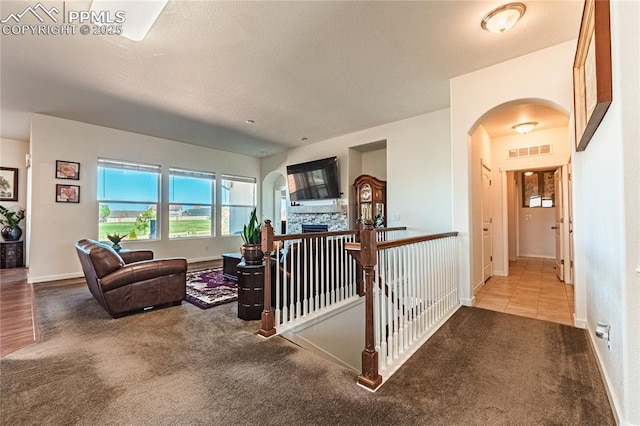 carpeted living area with arched walkways, a stone fireplace, baseboards, and visible vents