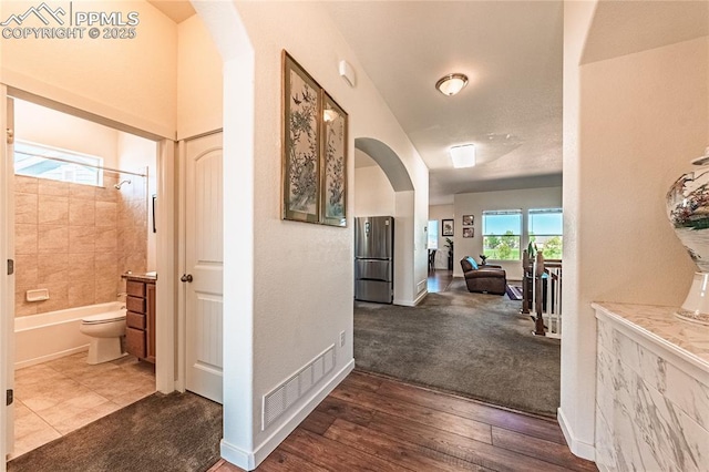 corridor featuring visible vents, baseboards, arched walkways, and dark wood-style floors
