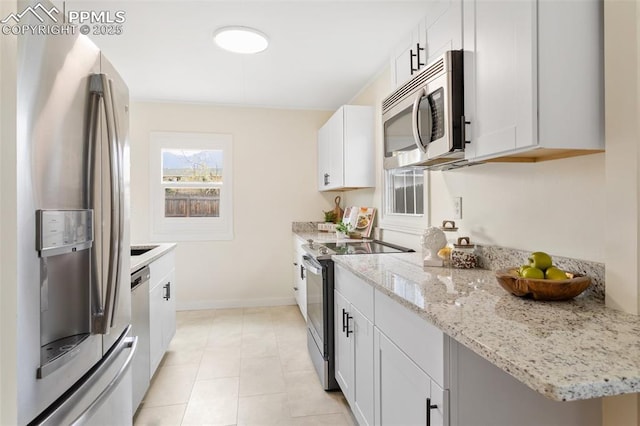 kitchen with stainless steel appliances, light stone countertops, white cabinetry, and baseboards