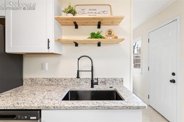 kitchen featuring open shelves, white cabinets, light stone counters, a sink, and dishwasher