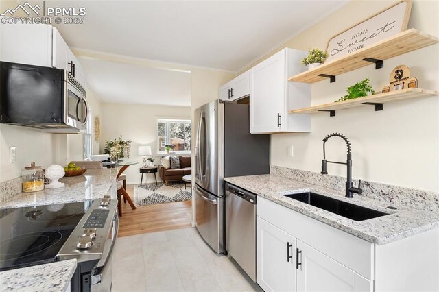 kitchen featuring open shelves, light stone countertops, a sink, stainless steel appliances, and white cabinetry