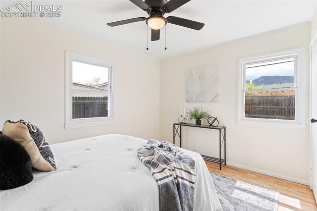 bedroom with a ceiling fan, baseboards, multiple windows, and wood finished floors