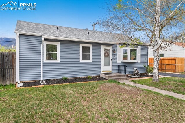 view of front of home featuring fence, a shingled roof, and a front lawn