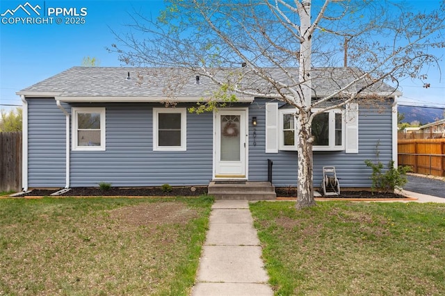 bungalow-style home with fence, roof with shingles, and a front lawn