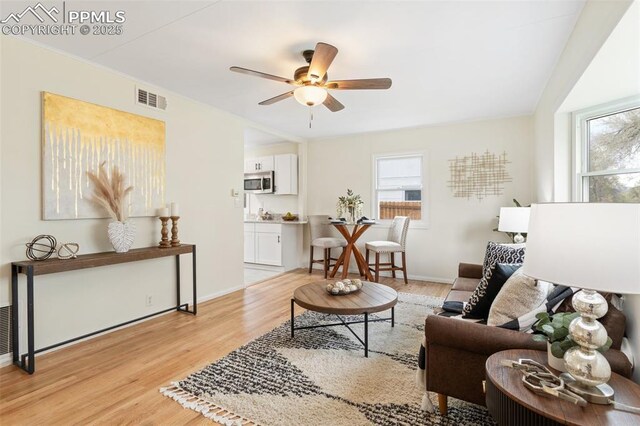 living area with baseboards, a ceiling fan, light wood-style flooring, and visible vents