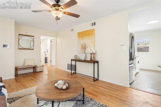 living area featuring baseboards, ceiling fan, light wood finished floors, and visible vents