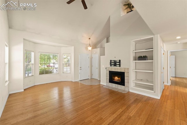 3245 Chestnut Glen Ln, Colorado Springs, CO 80918 - unfurnished living room with a ceiling fan, light wood finished floors, a tiled fireplace, built in shelves, and a towering ceiling