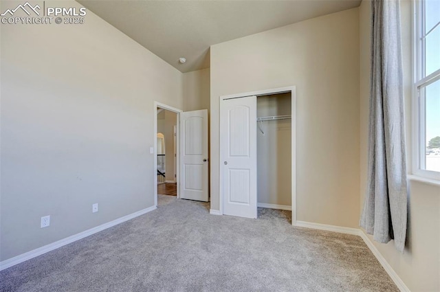 unfurnished bedroom featuring carpet floors, baseboards, vaulted ceiling, and a closet
