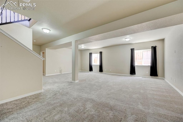 below grade area featuring baseboards, carpet, stairs, and a healthy amount of sunlight