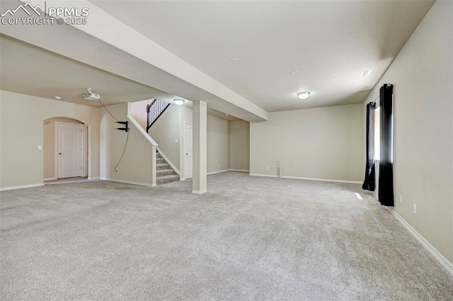 finished below grade area featuring baseboards, arched walkways, stairs, and light carpet