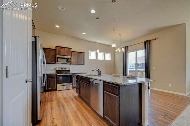 kitchen featuring dark brown cabinetry, appliances with stainless steel finishes, light wood-type flooring, a sink, and light stone counters