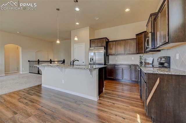 kitchen with a breakfast bar area, appliances with stainless steel finishes, arched walkways, light stone countertops, and wood finished floors