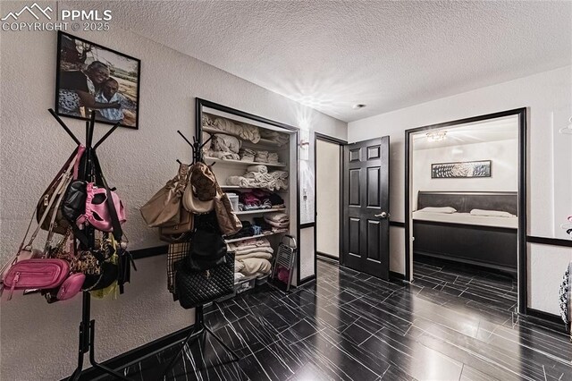 hall with baseboards, a textured ceiling, and a textured wall