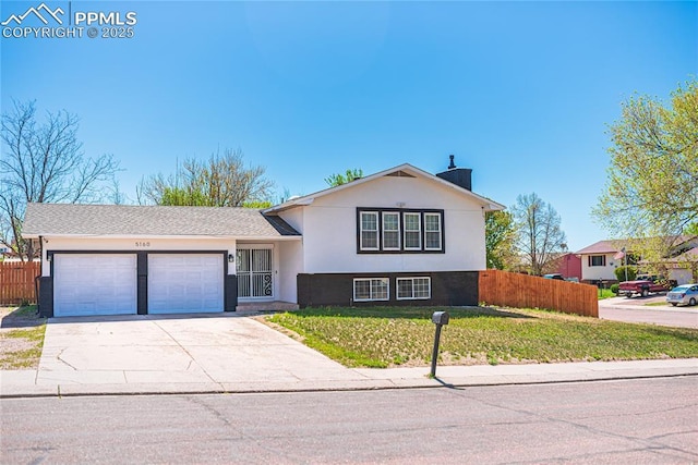 tri-level home featuring driveway, a front yard, fence, an attached garage, and stucco siding