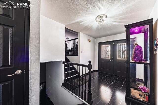 foyer entrance with baseboards, a textured ceiling, marble finish floor, and stairway