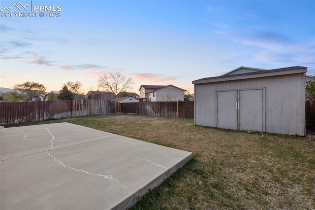 yard at dusk with an outdoor structure, a fenced backyard, and a storage shed