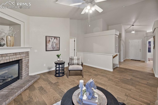 living area with baseboards, ceiling fan, wood finished floors, and a fireplace
