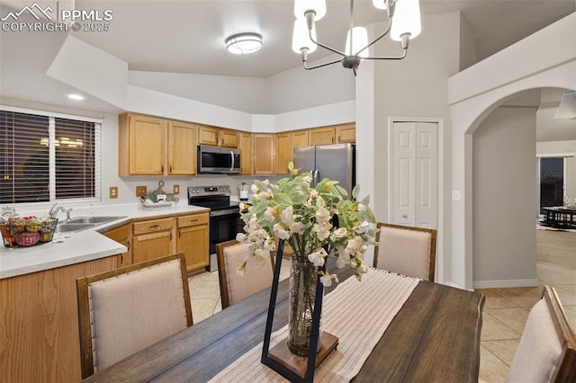 kitchen with arched walkways, a sink, light tile patterned floors, an inviting chandelier, and stainless steel appliances