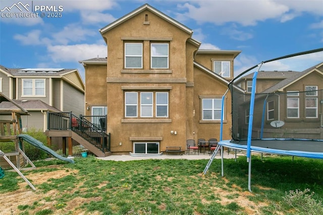 5019 Petrified Forest Trl, Colorado Springs, CO 80924 - back of house with a trampoline, stucco siding, stairs, and a lawn