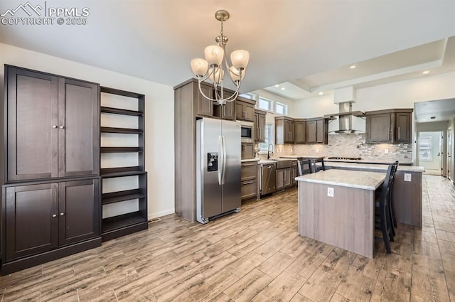 4157 Gray Fox Hts, Colorado Springs, CO 80922 - kitchen with a notable chandelier, light wood finished floors, wall chimney exhaust hood, stainless steel appliances, and decorative backsplash