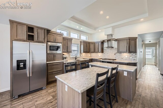 4157 Gray Fox Hts, Colorado Springs, CO 80922 - kitchen with light wood-style floors, wall chimney range hood, a center island, tasteful backsplash, and appliances with stainless steel finishes