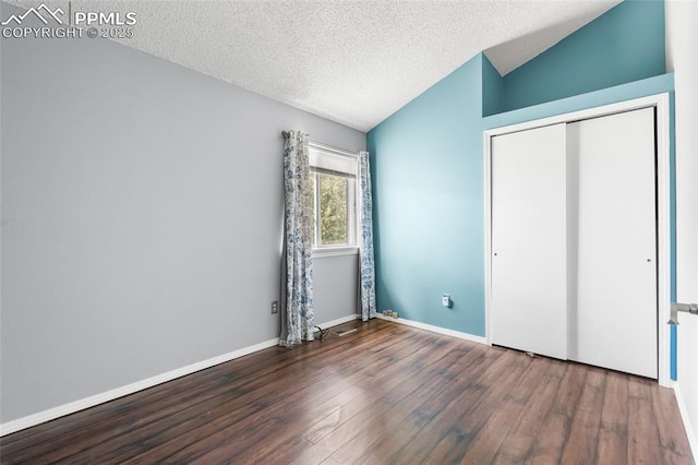 unfurnished bedroom with lofted ceiling, wood finished floors, a textured ceiling, a closet, and baseboards
