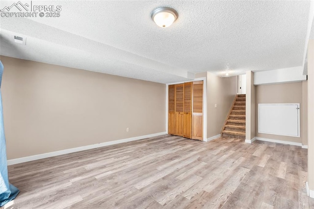 finished basement with a textured ceiling, stairway, light wood-style floors, and baseboards