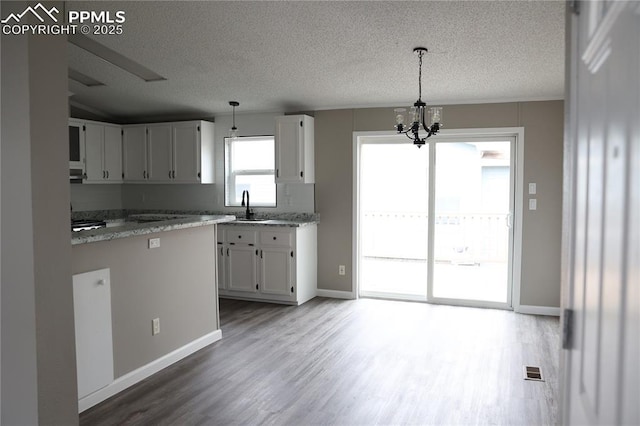 4663 Pine Marten Pt, Colorado Springs, CO 80922 - kitchen with an inviting chandelier, wood finished floors, a textured ceiling, and white cabinetry