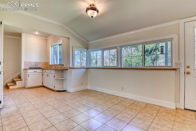 interior space with vaulted ceiling, decorative backsplash, light tile patterned floors, white cabinets, and baseboards