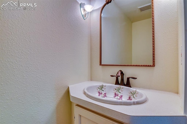 bathroom featuring visible vents, vanity, and a textured wall