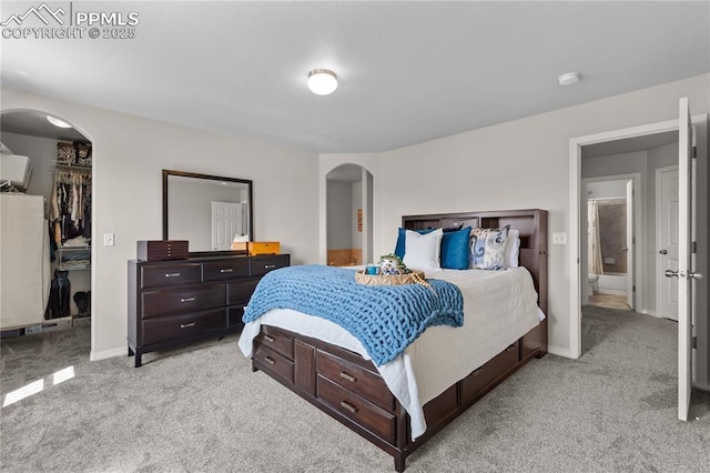 bedroom with light colored carpet, arched walkways, baseboards, and a spacious closet