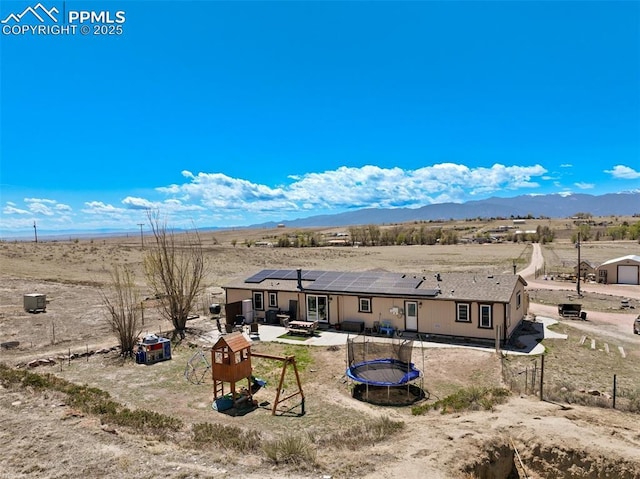 3235 S Meridian Rd, Colorado Springs, CO 80929 - rear view of property with a trampoline, an outdoor fire pit, a mountain view, and solar panels