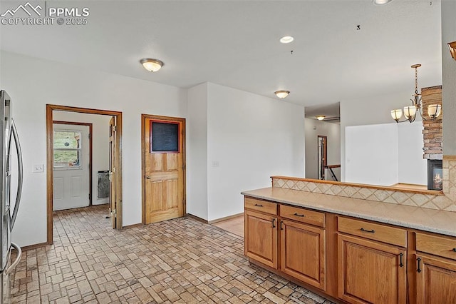 17880 Plains Edge Ct, Peyton, CO 80831 - kitchen featuring brown cabinets, stainless steel refrigerator, baseboards, brick patterned floor, and a peninsula