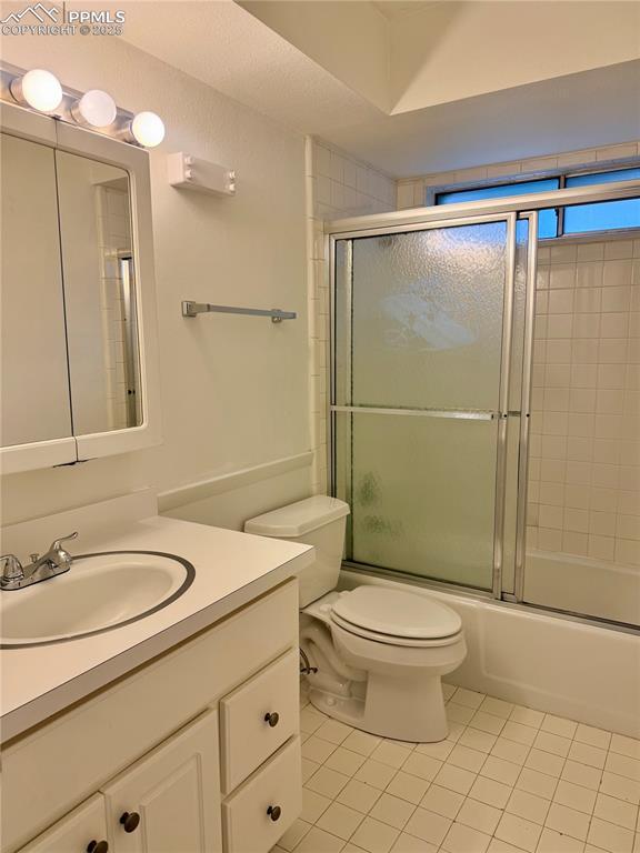 bathroom with toilet, tile patterned flooring, vanity, and shower / bath combination with glass door