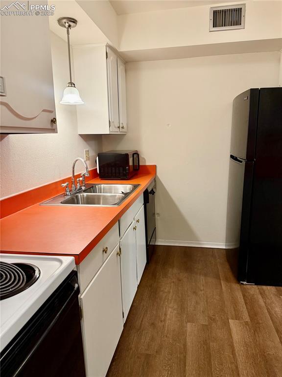 kitchen with a sink, white cabinetry, visible vents, dark wood-type flooring, and black appliances