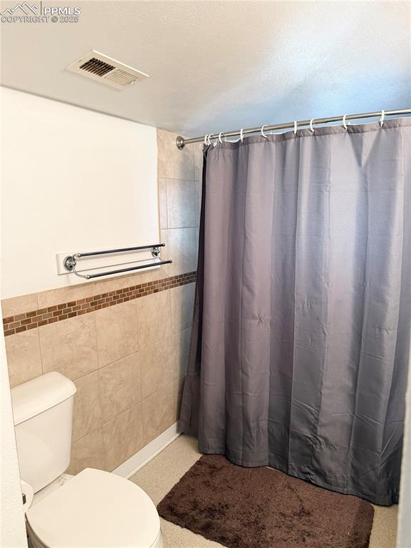 1322 Lincoln Ave, La Junta, CO 81050 - bathroom with visible vents, a shower with curtain, toilet, and tile walls