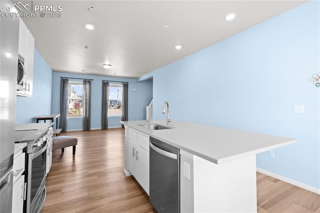 kitchen with a sink, white cabinetry, a center island with sink, stainless steel appliances, and light wood-type flooring
