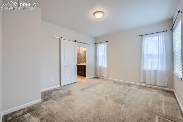 unfurnished bedroom with a barn door, baseboards, multiple windows, and light colored carpet