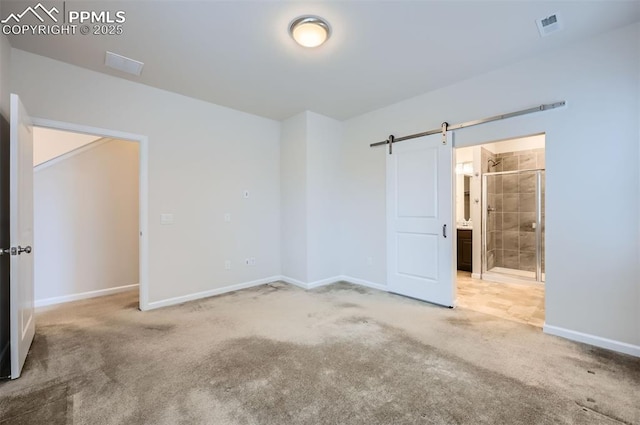 unfurnished bedroom with carpet flooring, baseboards, a barn door, and connected bathroom