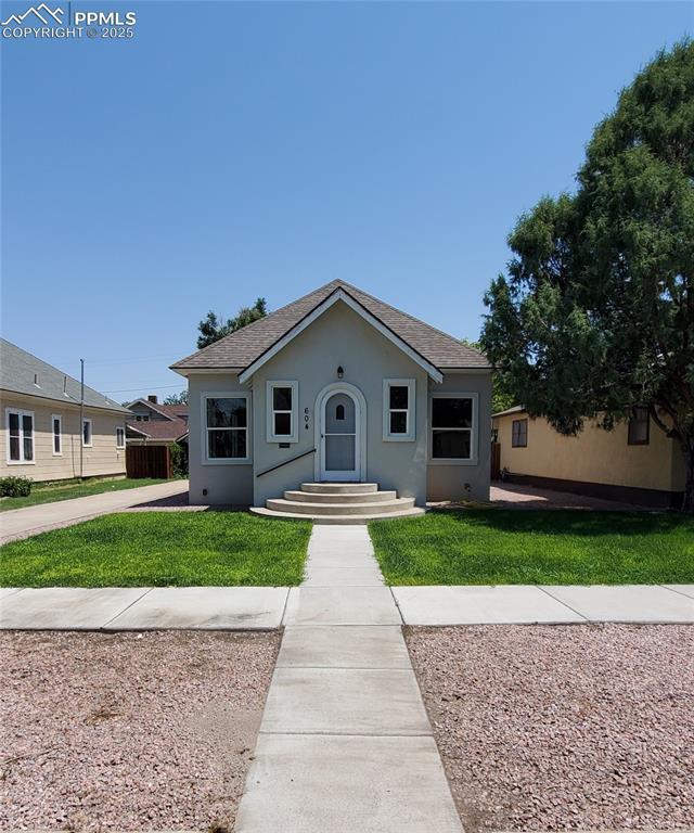 bungalow-style home featuring a shingled roof, stucco siding, and a front yard