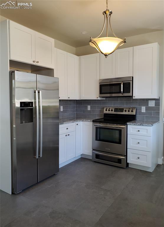 kitchen with light stone countertops, hanging light fixtures, stainless steel appliances, white cabinetry, and backsplash